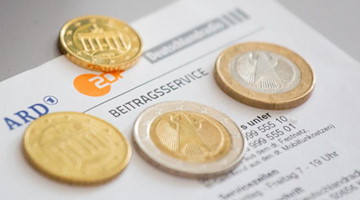 Euromünzen liegen auf einem Anschreiben zur Anmeldung für die Rundfunkgebühren, neben den Logo von ARD (l-r), ZDF und Deutschlandfunk. Foto: Fernando Gutierrez-Juarez/dpa-Zentralbild/dpa