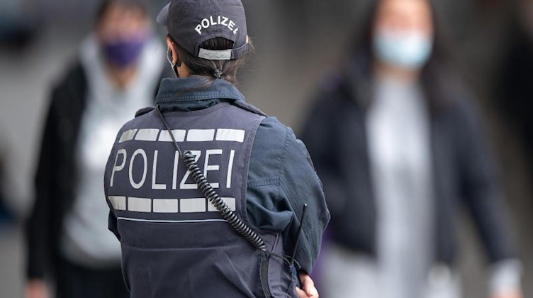 Eine Polizistin Blickt zu Passanten mit Masken. Foto: Sebastian Gollnow/dpa/Symbolbild