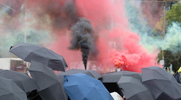 Teilnehmer einer linken Demonstration gehen eine Straße entlang und zünden Pyrotechnik. Foto: Sebastian Willnow/dpa-Zentralbild/dpa