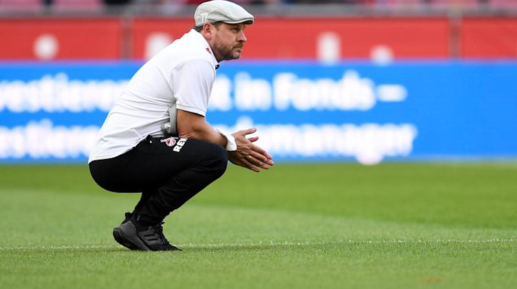 Kölns Trainer Steffen Baumgart hockt vor dem Spiel auf dem Rasen. Foto: Marius Becker/dpa