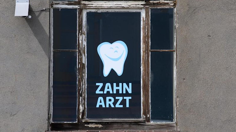 Zahnarzt steht an einem Fenster eines Hauses, in dem sich eine Zahnarztpraxis befindet, geschrieben. Foto: Robert Michael/dpa-Zentralbild/dpa