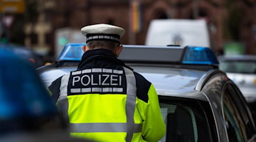 Ein Polizeibeamter steht zwischen zwei Einsatzfahrzeugen der Polizei. Foto: Philipp von Ditfurth/dpa/Symbolbild