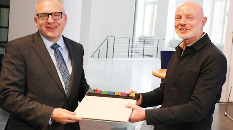 Oberbürgermeister Sven Schulze (l, SPD) überreicht Stefan Schmidtke ein Begrüssungsbuch. Foto: Bodo Schackow/dpa-Zentralbild/dpa