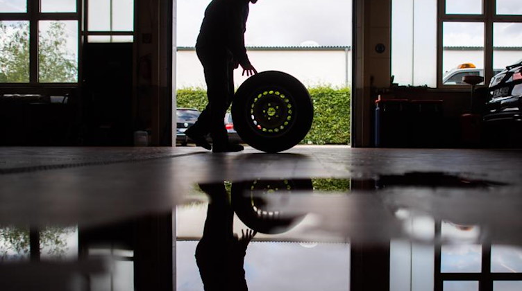Ein Auszubildender zum KfZ-Mechatroniker rollt einen Reifen durch eine Werkstatt. Foto: Julian Stratenschulte/dpa/Symbolbild