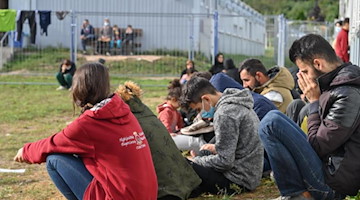 Migranten sitzen auf einer Wiese in einer Erstaufnahmeeinrichtung für Asylbewerber. Foto: Patrick Pleul/dpa-Zentralbild/ZB