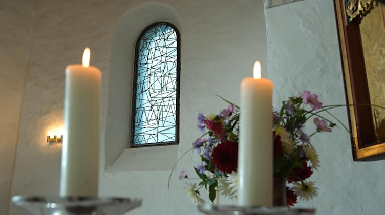 Kerzen brennen vor einem, der vom Künstler B. Muhr gestalteten modernen Kirchenfenster. Foto: Heiko Rebsch/dpa-Zentralbild/dpa
