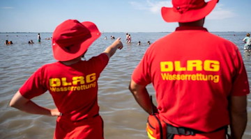 Mitglieder der DLRG stehen am Strand. Foto: Sina Schuldt/dpa/Archivbild