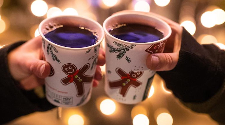 Zwei Besucherinnen eines Weihnachtsmarktes stoßen mit Glühwein an. Foto: Christoph Schmidt/dpa/Symbolbild