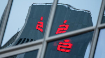 Das Sparkassen-Logo spiegelt sich in einem Fenster. Foto: Andreas Arnold/dpa/Symbolbild