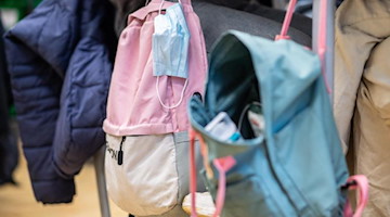 Ein Mund-Nasen-Schutz hängt in einem Klassenzimmer am Rucksack. Foto: Guido Kirchner/dpa/Symbolbild