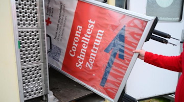 Mitarbeiter des DRK Dresden verladen ein Hinweisschild für ein mobiles Corona-Testzentrum. Foto: Robert Michael/dpa-Zentralbild/dpa/Archivbild