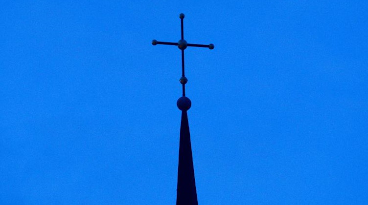 Das Kreuz einer Kirche ist in der Abenddämmerung zu sehen. Foto: Friso Gentsch/dpa/Symbolbild