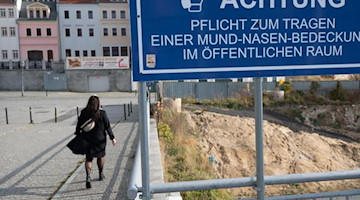 Eine Passantin geht in Görlitz über die deutsch-polnische Grenze hinter einem Schild mit dem Hinweis auf die Maskenpflicht. Foto: Sebastian Kahnert/dpa-Zentralbild/dpa