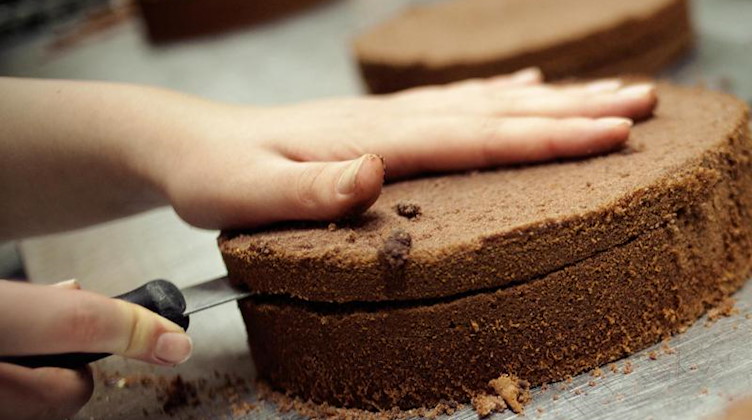 Eine angehende Konditorin schneidet einen Kuchenboden durch. Foto: picture alliance/dpa/Symbolbild