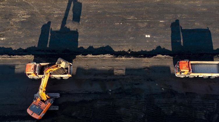Ein Bagger und zwei Lkw werfen Schatten auf einer Baustelle. Foto: Jan Woitas/dpa-Zentralbild/dpa/Symbolbild