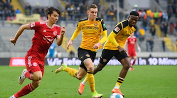 Dynamos Julius Kade (M) und Michael Akoto gegen Düsseldorfs Ao Tanaka (l). Foto: Robert Michael/dpa-Zentralbild/dpa