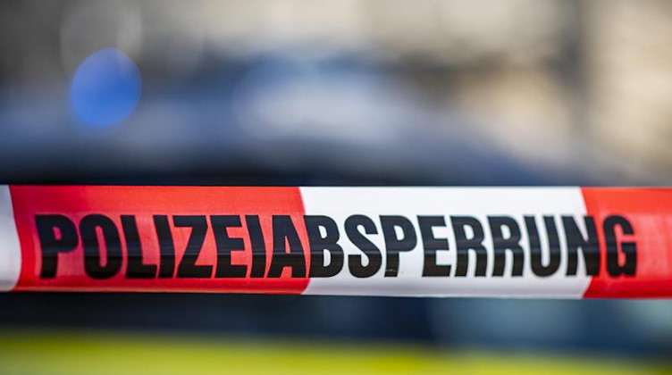 Ein Absperrband mit der Aufschrift «Polizeiabsperrung» ist vor einem Polizeiwagen aufgespannt. Foto: David Inderlied/dpa/Illustration