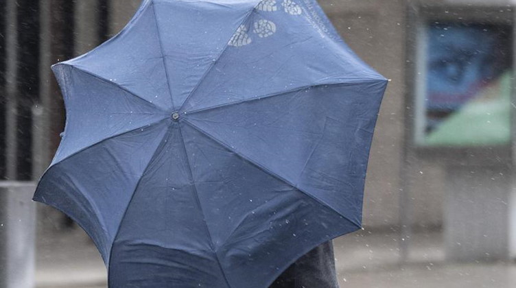 Bei Regenwetter kämpft sich ein Passant mit Regenschirm durch die Innenstadt. Foto: Boris Roessler/dpa/Symbolbild