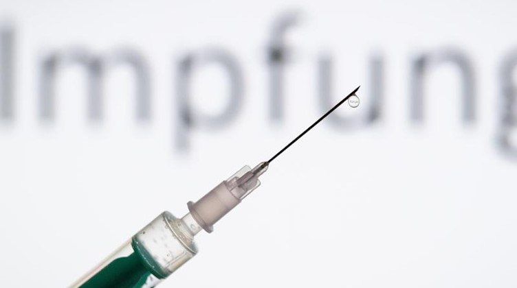 Eine Spritze wird vor den Schriftzug «Impfung» gehalten. Foto: Friso Gentsch/dpa/Symbolbild