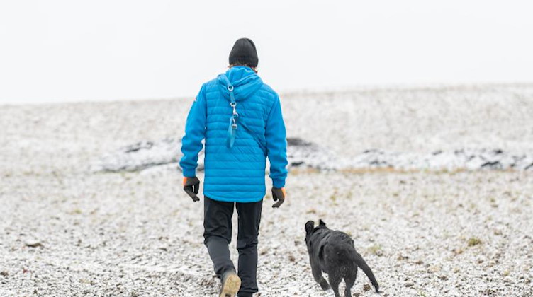Ein Mann geht mit einem Hund auf einem verschneiten Feld in der Sächsischen Schweiz spazieren. Foto: Daniel Schäfer/dpa-Zentralbild/dpa