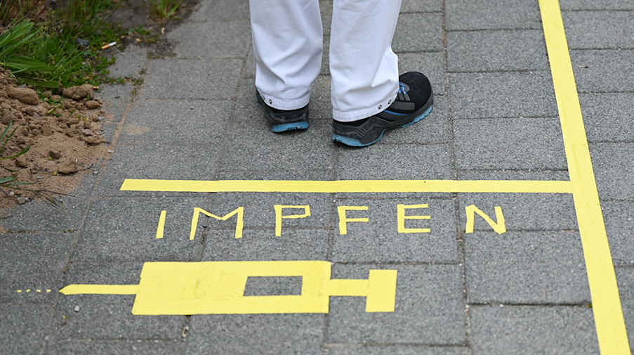 Ein Mann steht an einem Covid-19-Impfcenter hinter der Bodenaufschrift "Impfen". / Foto: Arne Dedert/dpa/POOL/dpa/Symbolbild