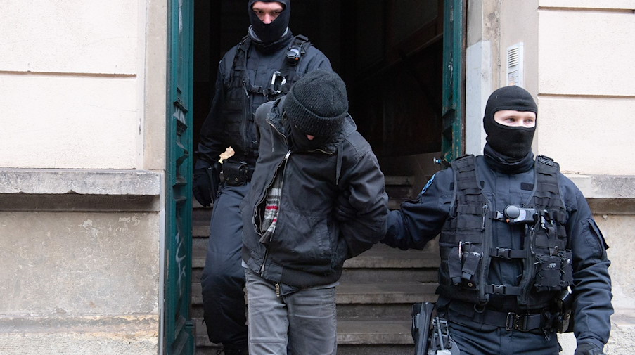Polizisten führen bei einer Razzia einen Tatverdächtigen aus einem Hauseingang. / Foto: Sebastian Kahnert/dpa-Zentralbild/dpa