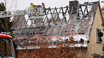 Von einer Drehleiter aus sucht ein Feuerwehrmann nach Glutnestern im Dachstuhl des Hauses. / Foto: Jan Woitas/dpa-Zentralbild/dpa