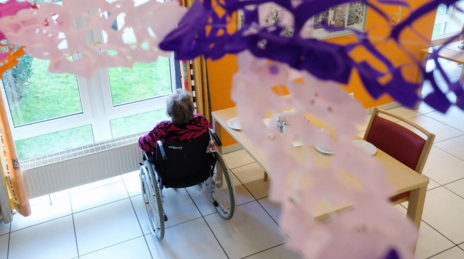 Die Bewohnerin eines Pflegeheimes mit Faschingsdekoration im Vordergrund sitz in einem Rollstuhl und blickt aus dem Fenster. / Foto: Sebastian Willnow/dpa-Zentralbild/dpa/Bildarchiv