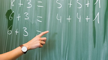 Eine Lehrerin schreibt in einer Schule an eine Tafel. / Foto: Julian Stratenschulte/dpa/Symbolbild
