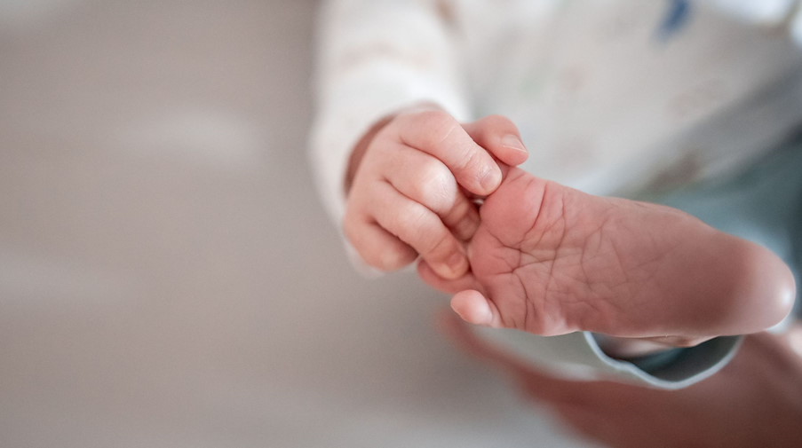 Ein Baby greift mit den Fingern nach seinem Fuß. / Foto: Fabian Strauch/dpa/Symbolbild