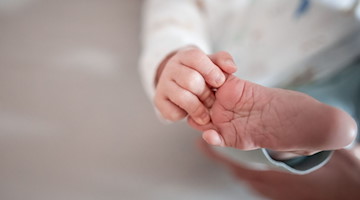 Ein Baby greift mit den Fingern nach seinem Fuß. / Foto: Fabian Strauch/dpa/Symbolbild