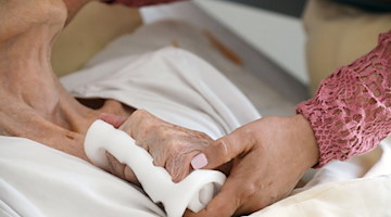 Eine Pflegeschwester hält die Hand einer alten Heimbewohnerin. / Foto: Bodo Schackow/dpa-Zentralbild/dpa/Symbolbild