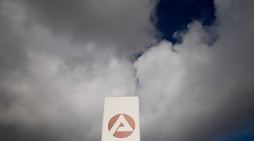 Wolken ziehen über ein Schild der Agentur für Arbeit. / Foto: Carsten Koall/dpa/Symbolbild