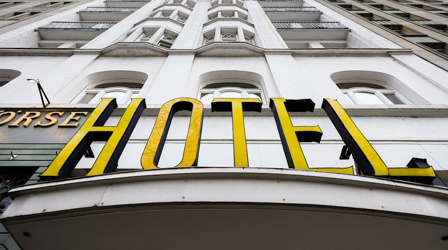Ein beleuchteter Schriftzug eines Hotels ist über dem Eingang angebracht. / Foto: Ulrich Perrey/dpa/Bildarchiv