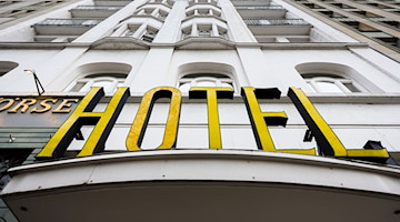 Ein beleuchteter Schriftzug eines Hotels ist über dem Eingang angebracht. / Foto: Ulrich Perrey/dpa/Bildarchiv