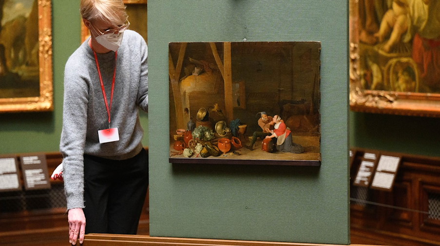 Eine Mitarbeiterin schiebt das Gemälde „Ein Alter umarmt die Magd im Stall“ an seine Position. / Foto: Robert Michael/dpa-Zentralbild/dpa
