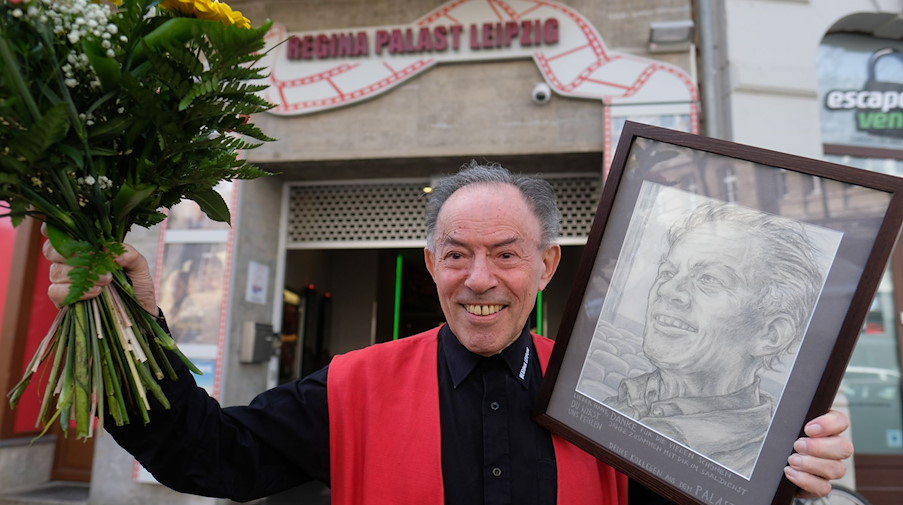 Hans Höher, Eisverkäufer im Kino, steht mit Blumen und einem Porträt vor dem Regina-Palast. / Foto: Sebastian Willnow/dpa-Zentralbild/dpa