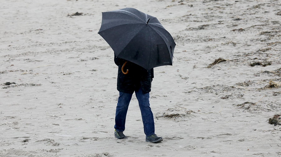 Ein Spaziergänger geht bei Regen und Wind an einem Strand entlang. / Foto: Bernd Wüstneck/dpa-Zentralbild/dpa/Symbolbild