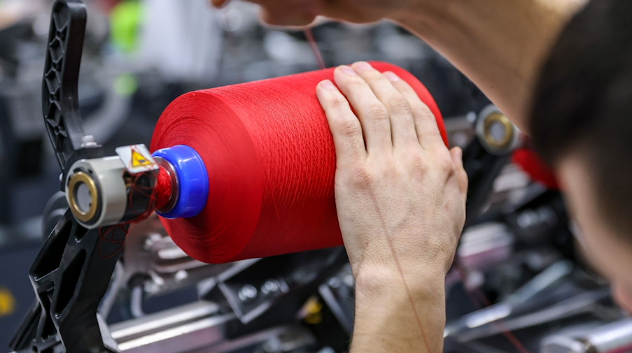 Ein Mitarbeiter wechselt in der Spulerei der OTEX Textilveredlung GmbH eine Spule mit farbigem Garn. / Foto: Jan Woitas/dpa-Zentralbild/dpa