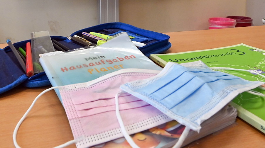 Masken liegen in einem Klassenzimmer auf einem Schulbuch. / Foto: Patrick Pleul/dpa-Zentralbild/dpa/Symbolbild