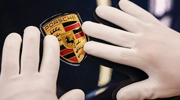 Ein Mitarbeiter des Leipziger Porsche Werks befestigt das Wappen an einem Porsche Macan. / Foto: Jan Woitas/dpa-Zentralbild/dpa/Symbolbild