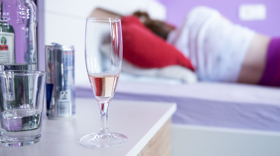Eine Frau liegt in ihrem Bett, neben dem Flaschen und Gläser mit Alkohol stehen. / Foto: Silas Stein/dpa/Symbolbild