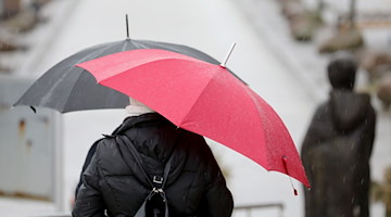 Passanten mit Regenschirmen gehen über eine Promenade. / Foto: Bernd Wüstneck/dpa-Zentralbild/dpa/Symbolbild