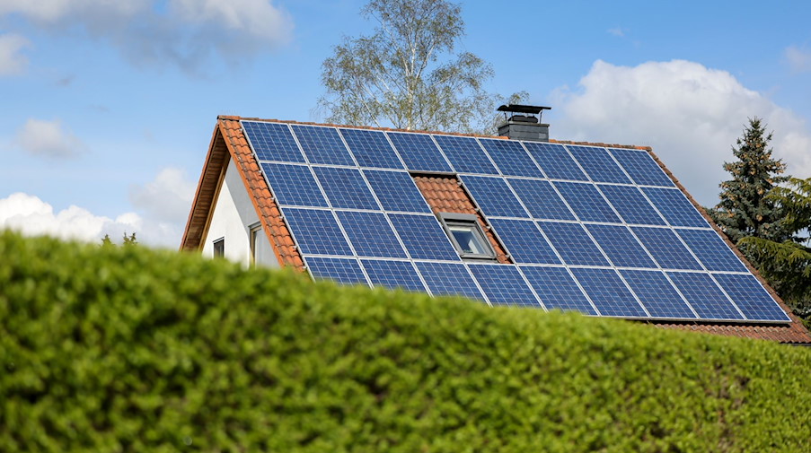 Ein Einfamilienhaus mit Solarpaneelen auf dem Dach steht hinter einer grünen Hecke. / Foto: Jan Woitas/dpa-Zentralbild/dpa/Symbolbild