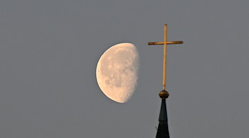 Der Mond steht im Morgenlicht hinter einem Kreuz auf einem Kirchturm. / Foto: Bernd Weißbrod/dpa/Symbolbild