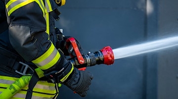Ein Mitglied der Feuerwehr spritzt aus einem Schlauch mit Wasser. / Foto: David Inderlied/dpa/Symbolbild