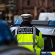 Ein Polizeibeamter steht zwischen zwei Einsatzfahrzeugen der Polizei. / Foto: Philipp von Ditfurth/dpa/Symbolbild