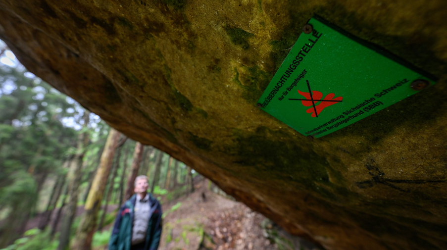 Ein Schild „Freiübernachtungsstelle“ ist an einem Felsen über einer offiziellen Boofe angeschraubt. / Foto: Robert Michael/dpa