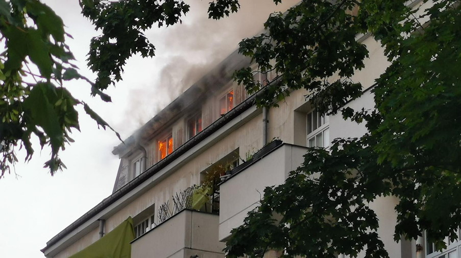Flammen sind an den Fenstern bei einem Dachstuhlbrand in einem Wohngebäude zu sehen. / Foto: -/Feuerwehr Dresden/dpa