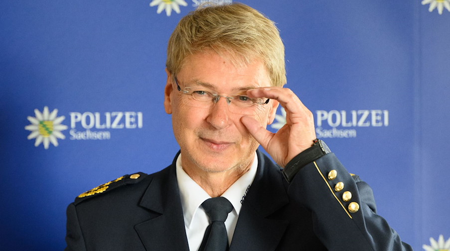 Lutz Rodig steht vor einer blauen Wand mit dem Logo der Polizei Sachsen. / Foto: Robert Michael/dpa